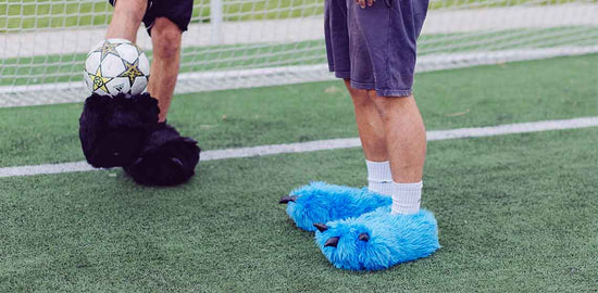 Zwei Personen mit Monster Tatzenhausschuhen auf Fußballfeld