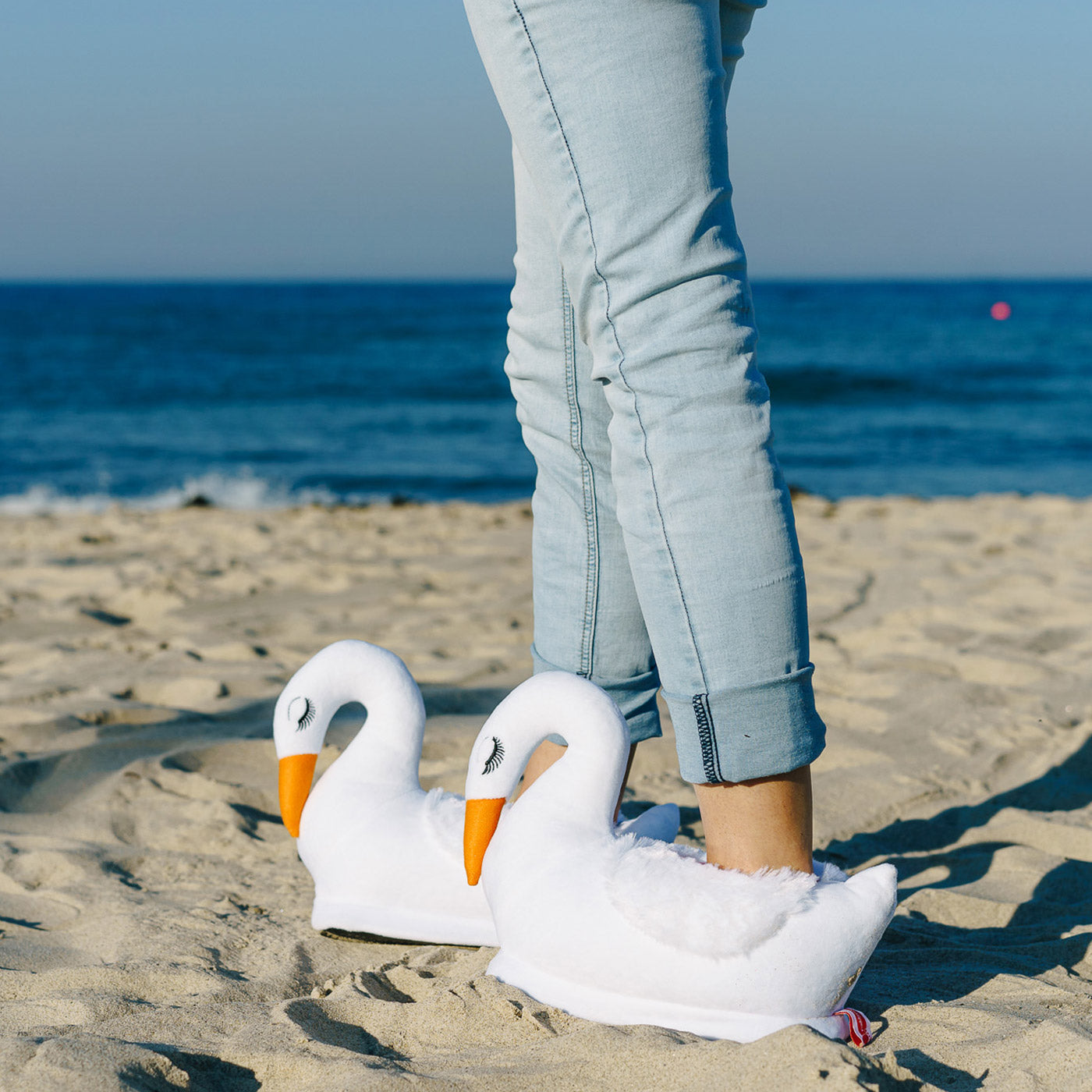 Person am Strand trägt weisse Schwan Hausschuhe