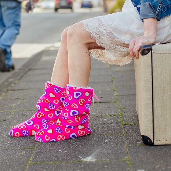 Person sitzt auf Koffer und trägt Plüsch Boots pink mit Herzen